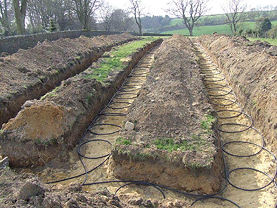 Ground-level view of trenches in a field with coiled black geothermal heat pump tubing laid out for installation.