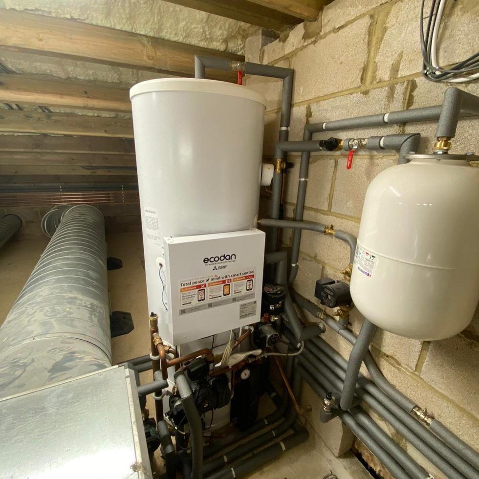 An Ecodan heat pump unit with a white cylindrical water tank and attached expansion vessel in an unfinished attic space.