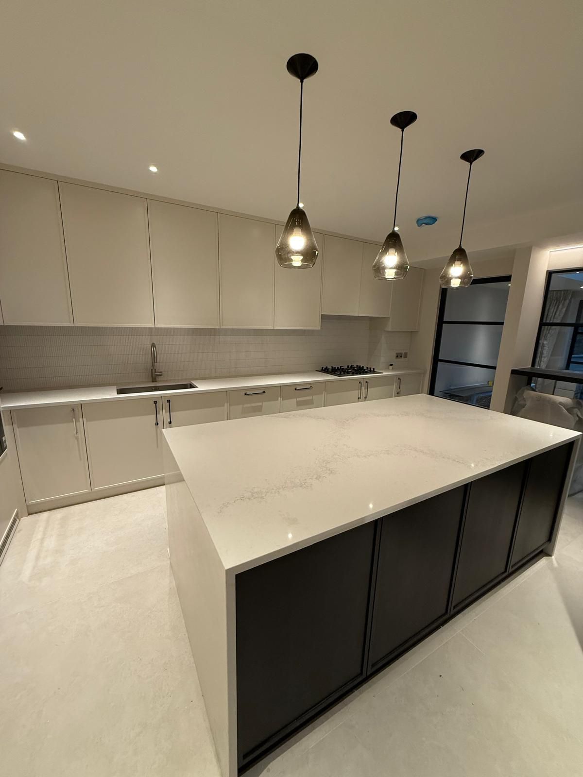 Modern kitchen featuring a white island with dark cabinetry, light countertops, and three hanging pendant lights.