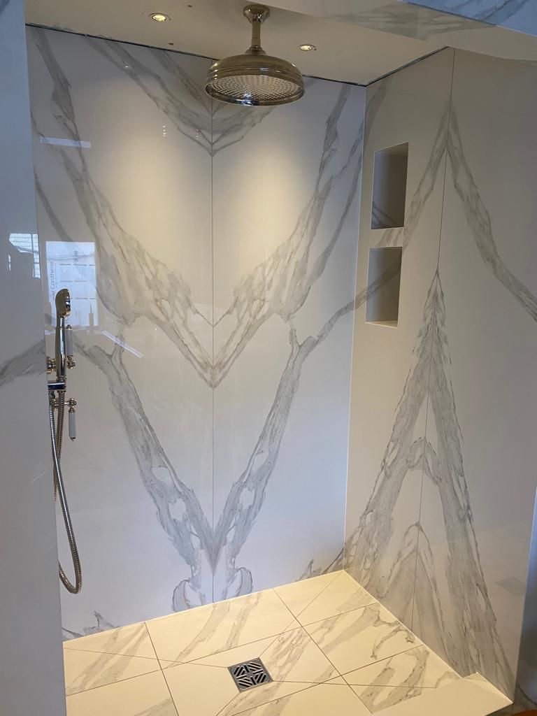 A luxurious walk-in shower featuring white marble walls with dramatic grey veining, a rainfall showerhead, and tiled floor.