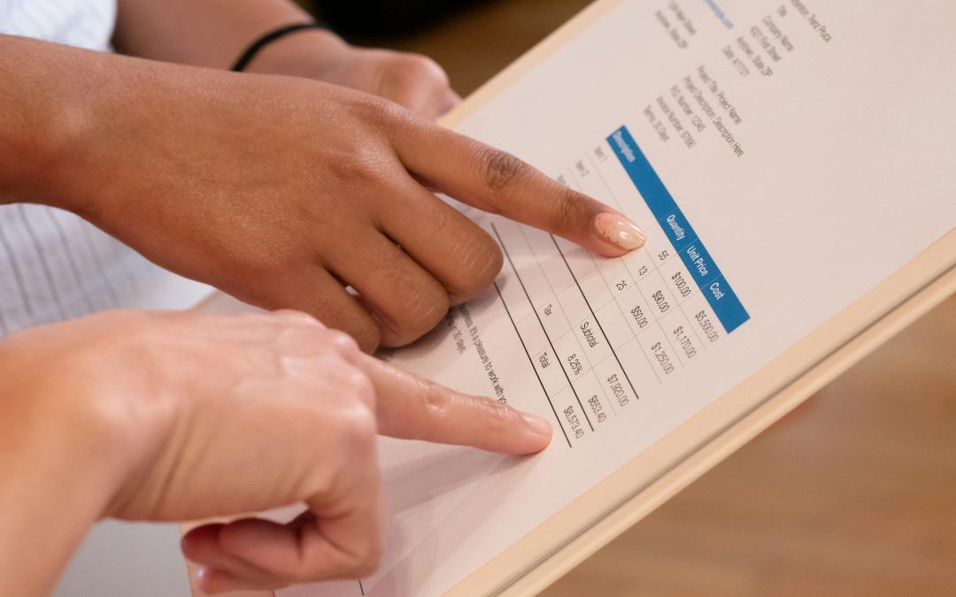 Two individuals point to data on a printed document, discussing information in a professional setting.