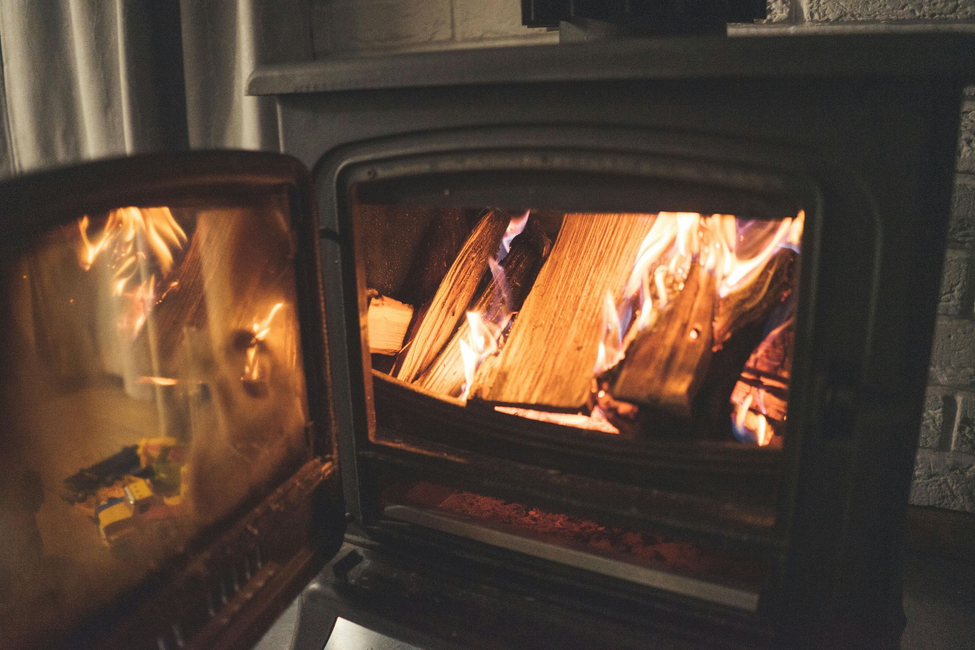 A wood-burning stove with an open door, showing pieces of wood burning with bright orange flames inside.