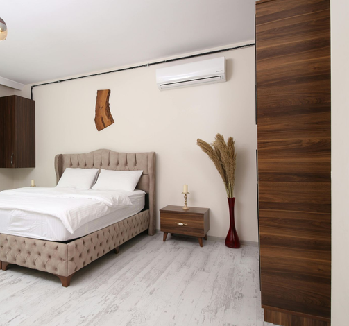 A bedroom featuring a beige tufted bed, a dark wood nightstand, a floor vase with dried plants, and a dark wood wardrobe.