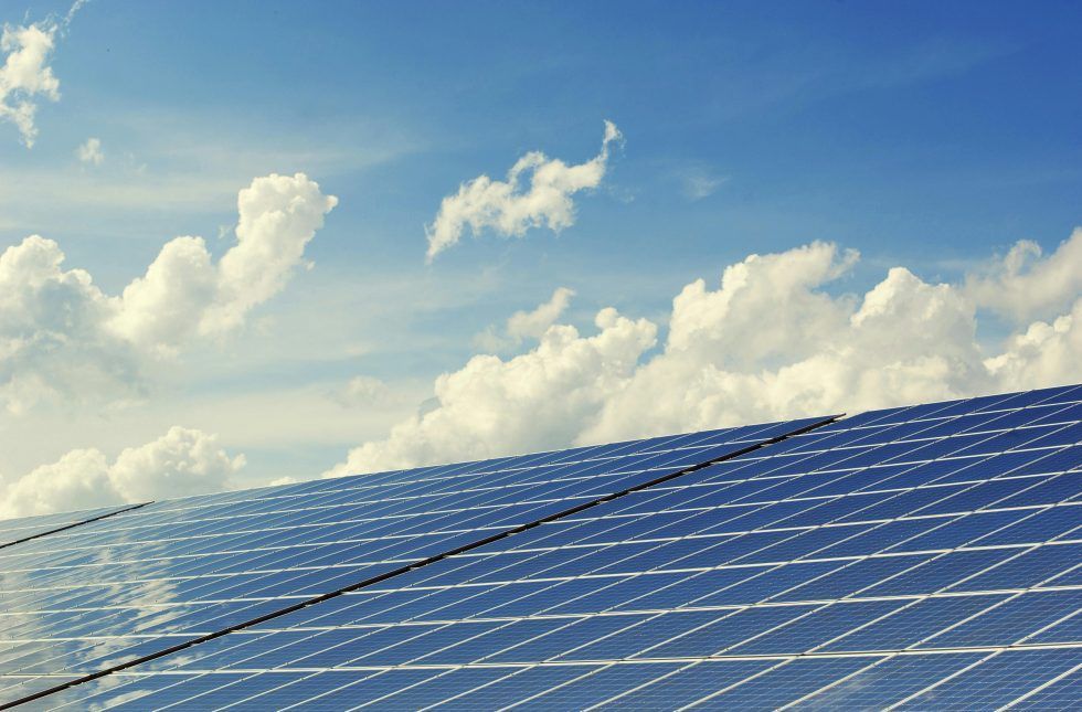 Solar panels tilted toward a bright blue sky filled with fluffy white clouds.