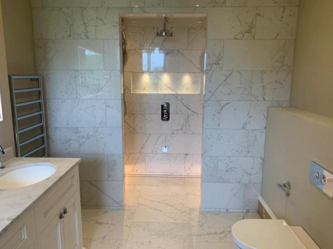 A modern bathroom featuring a white marble walk-in shower with a recessed shelf, a vanity with a sink, and a toilet.