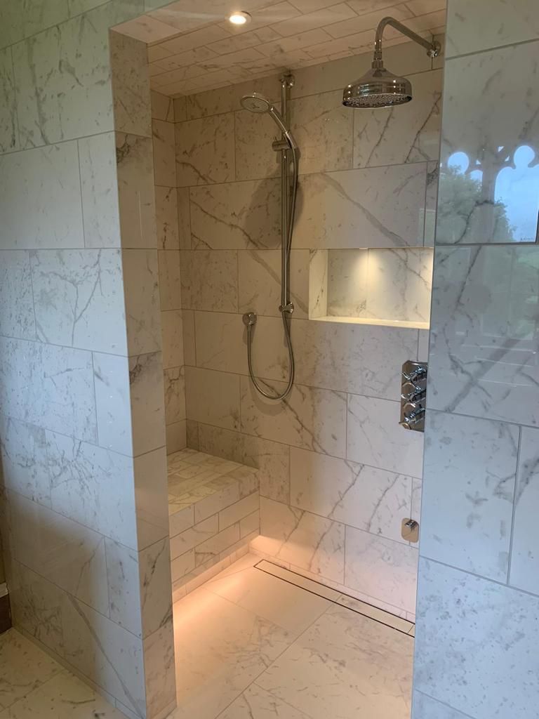 Modern walk-in shower with marble tile walls, a built-in bench, overhead and handheld showerheads, and recessed lighting.