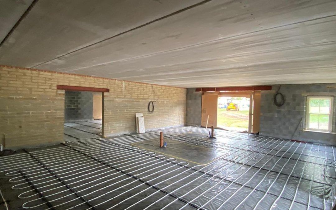 An interior view of a room under construction with radiant floor heating pipes installed over a concrete floor and walls.