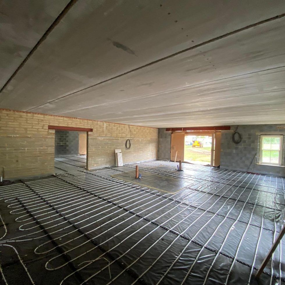 Construction site interior with radiant heating tubing installed on a black underlayment across a concrete floor.