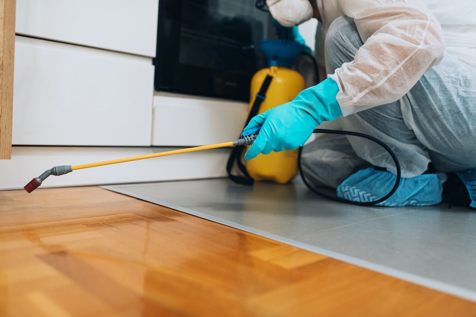 Person in protective gear spraying insecticide in a kitchen.