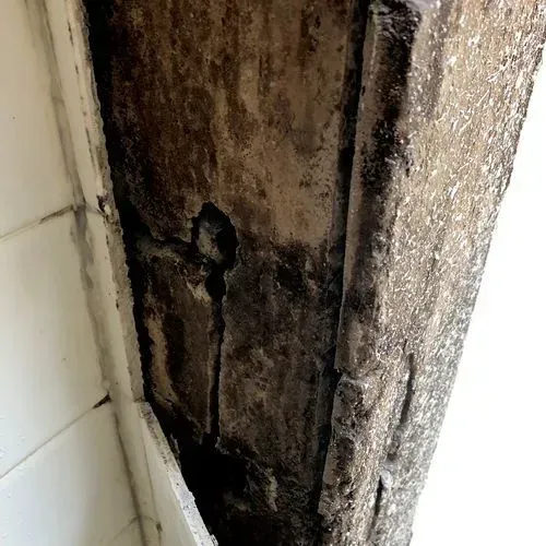 Close-up of a damaged, weathered concrete beam with a dark, textured surface, possibly showing water damage.
