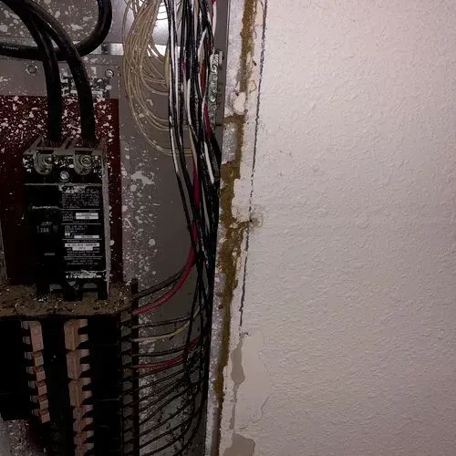 Electrical panel with exposed wires and wall damage.