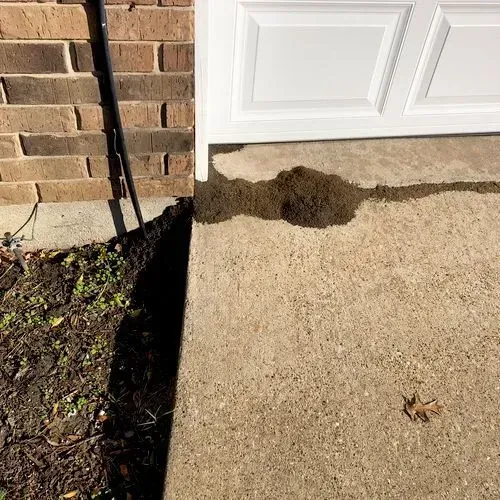 A pile of dirt and water spreads from the base of a white garage door onto a concrete slab.