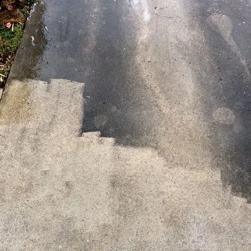 Concrete walkway partially cleaned, showing contrast between dirty and clean areas.
