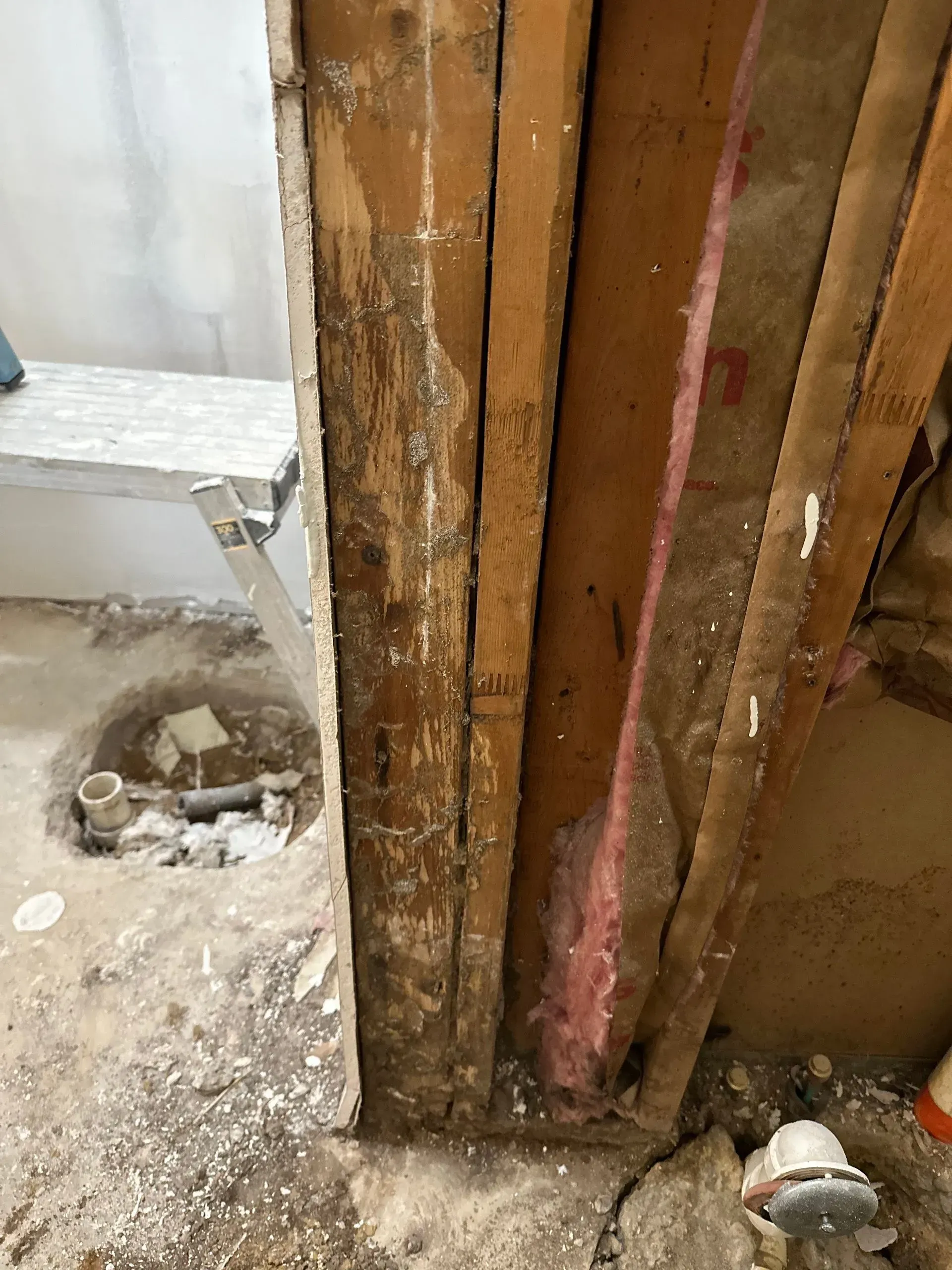 Exposed wall studs, insulation, and plumbing. Construction debris and unfinished floor visible.