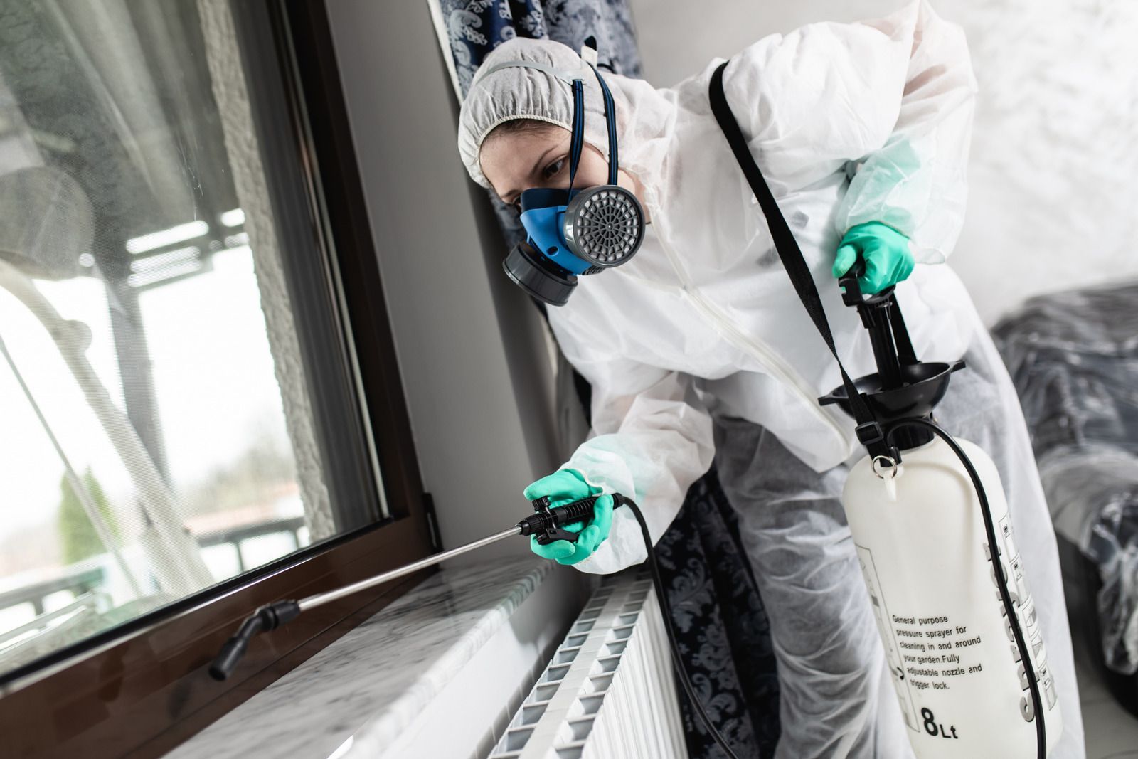 Person in protective suit spraying insecticide near window.