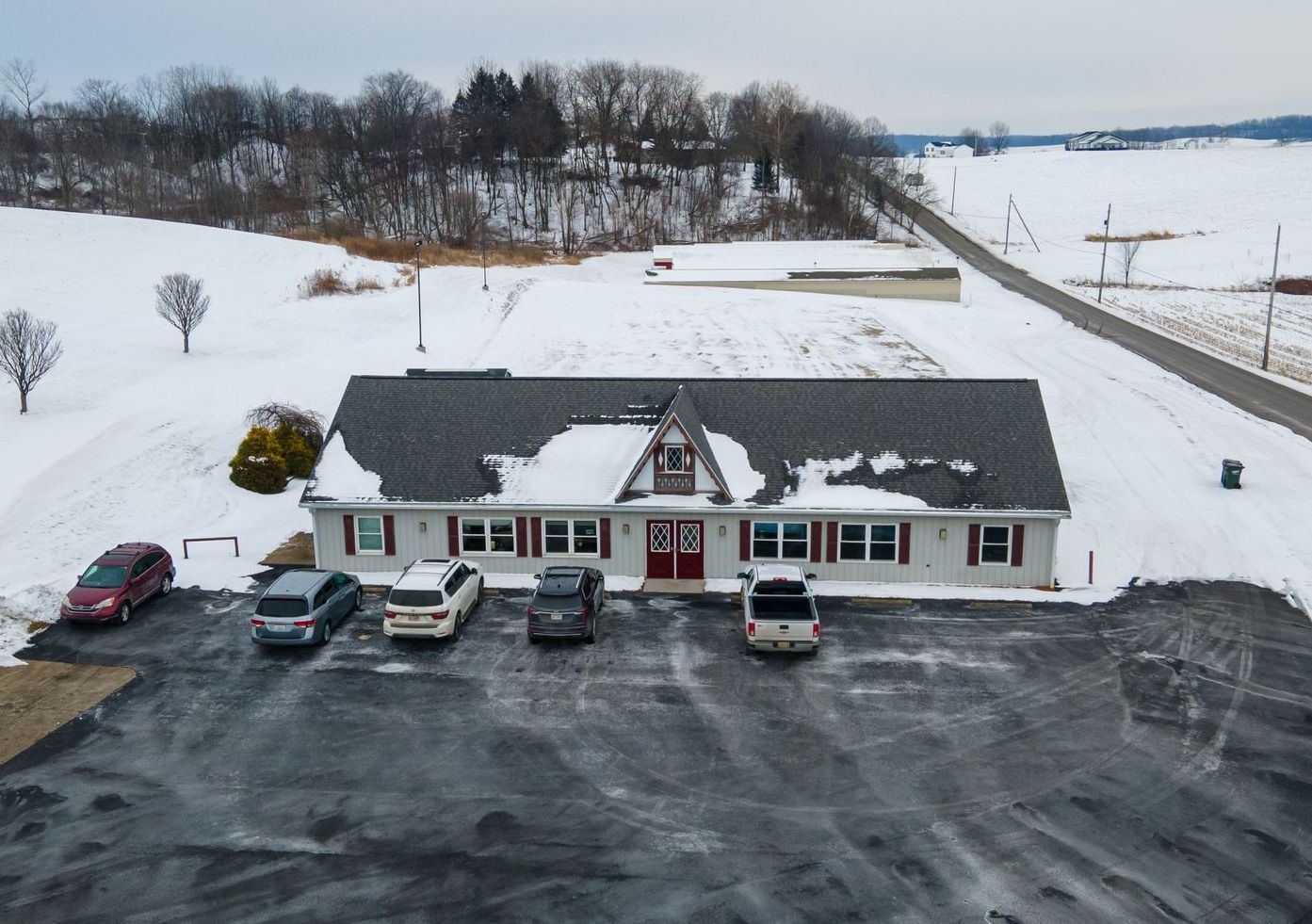 Snow-covered building with cars parked out front, set in a rural winter landscape.