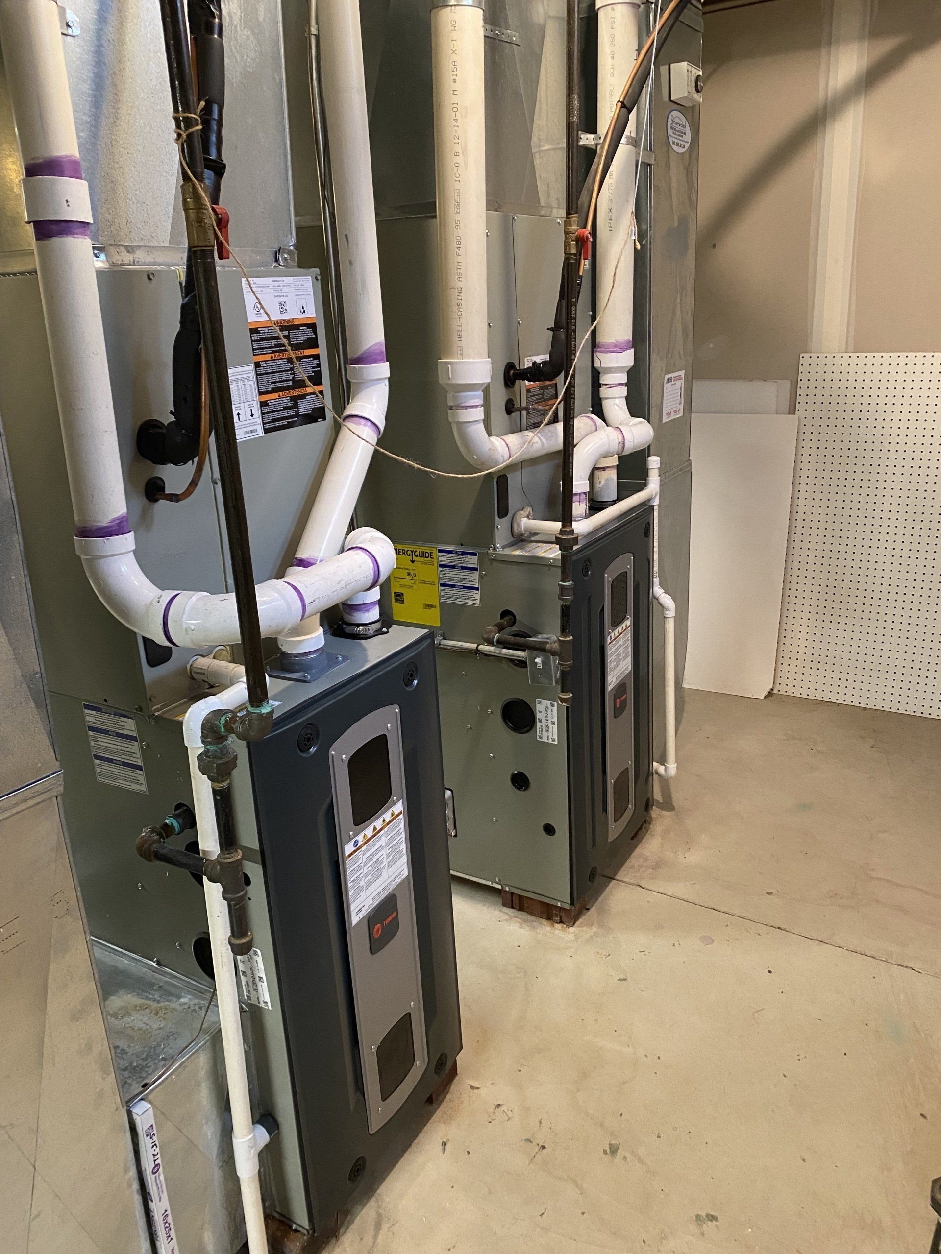 Two air conditioners are sitting next to each other in a basement.