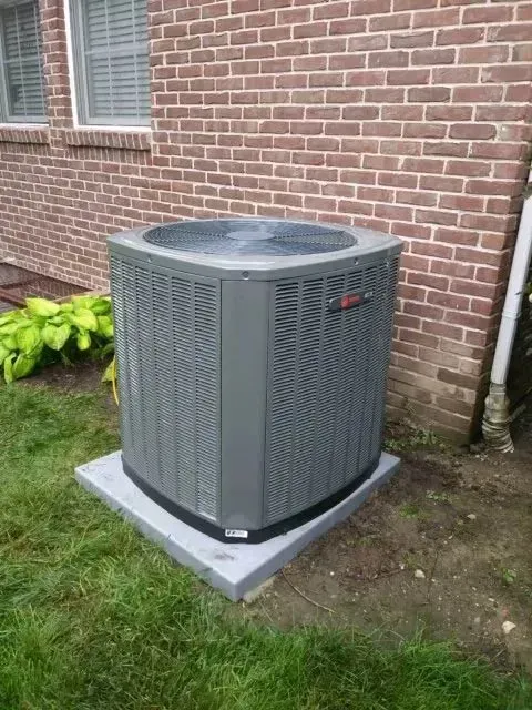 An air conditioner is sitting outside of a brick house.