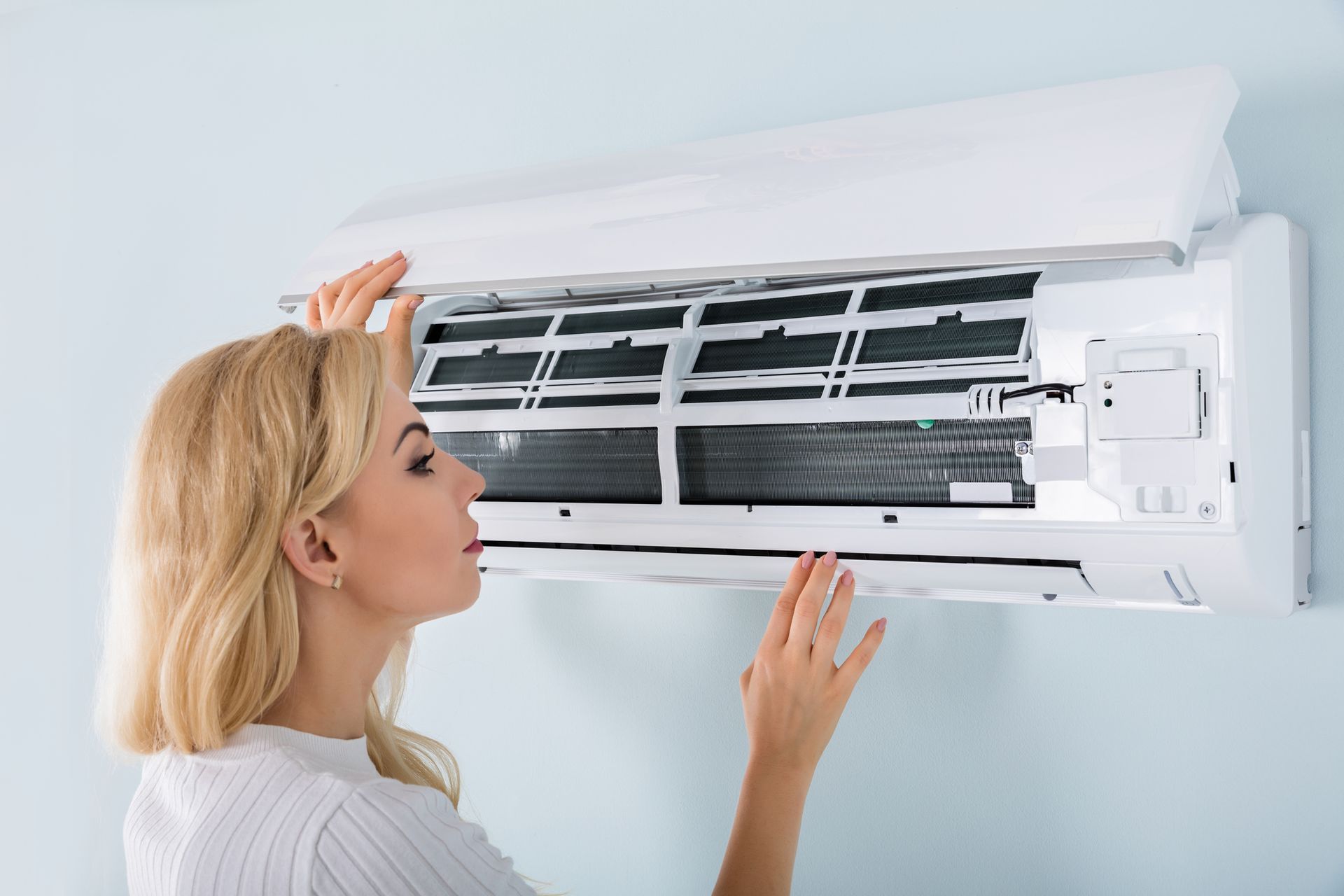 A woman is cleaning a wall mounted air conditioner.