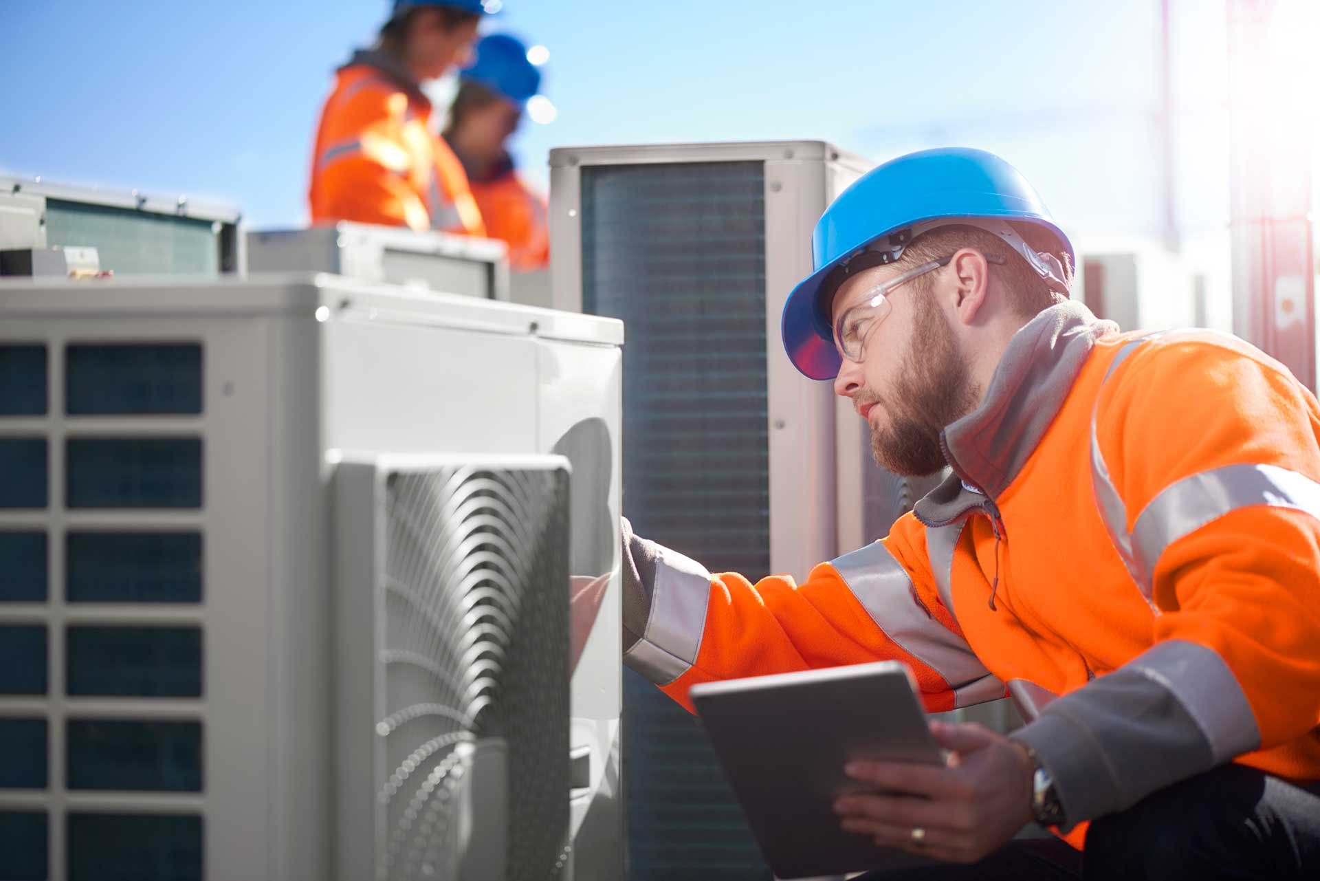 A man is using a tablet while working on an air conditioner.