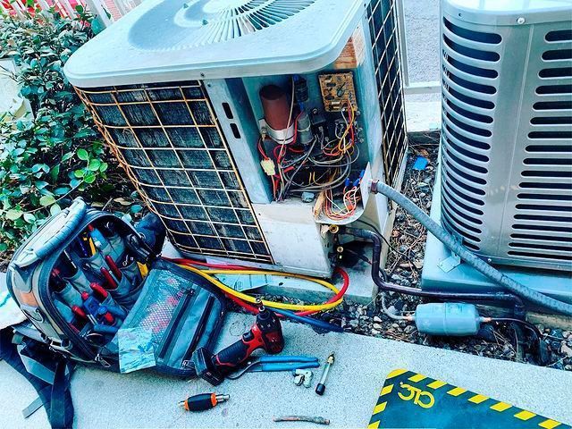 A broken air conditioner is sitting on the ground next to a tool bag.