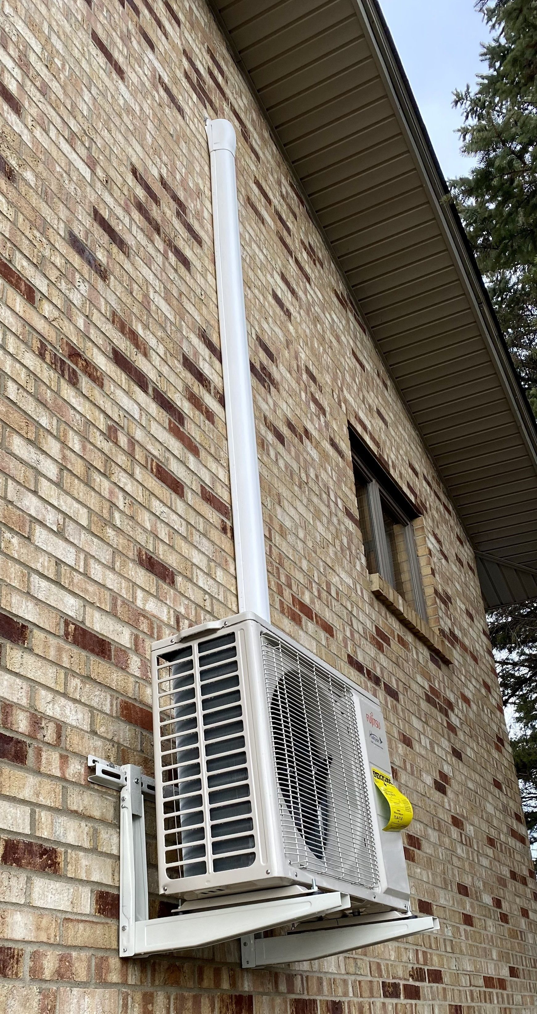 An air conditioner is mounted on the side of a brick building.