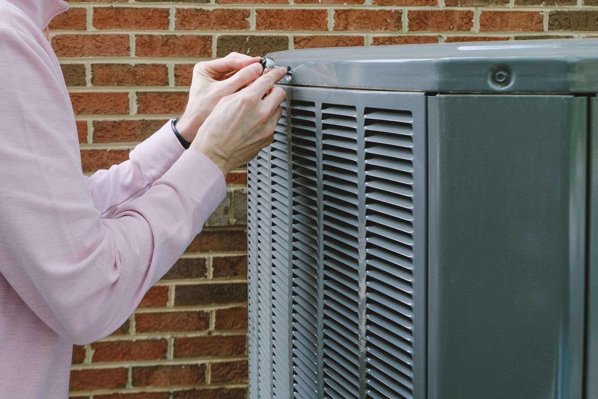 A man is fixing an air conditioner outside of a brick building.