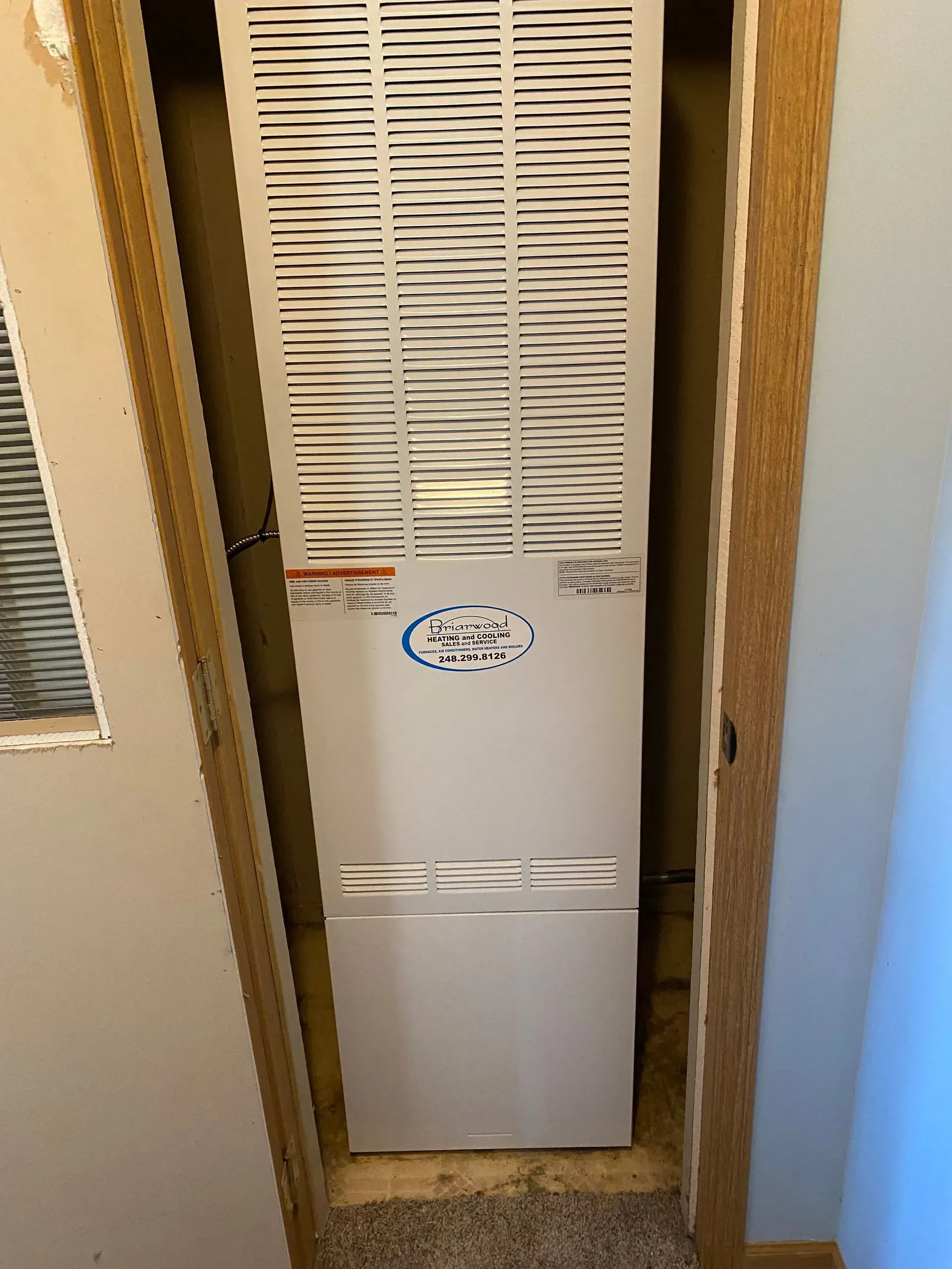 A white air conditioner is sitting in a closet next to a door.