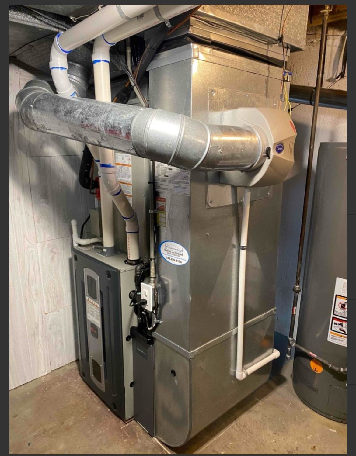 A furnace and water heater in a basement setting with ductwork and pipes.