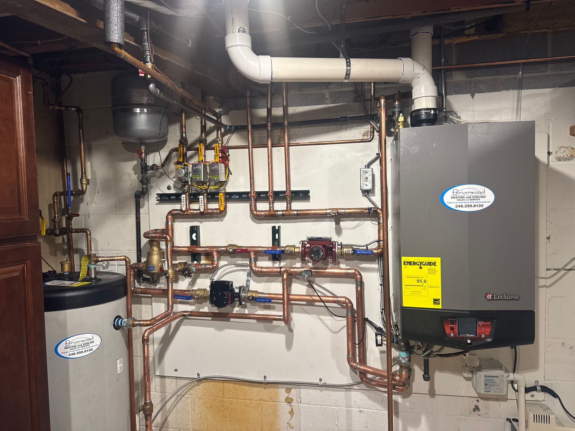 Copper pipes and a boiler system installed on a white basement wall.