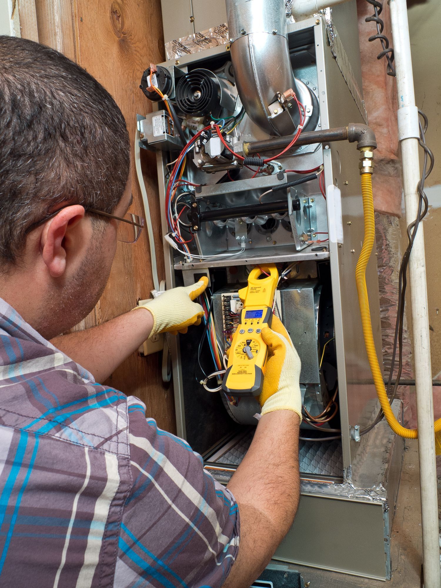 A man is working on an air conditioner with a digital multimeter.