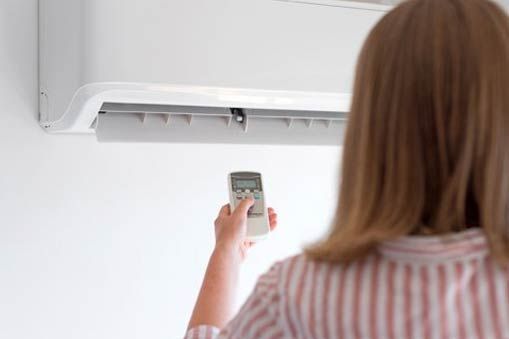 Woman Holding Remote for Air Condition — Rochester Hills, MI — Briarwood Heating & Cooling Woman Holding Remote for Air Condition — Rochester Hills, MI — Briarwood Heating & Cooling