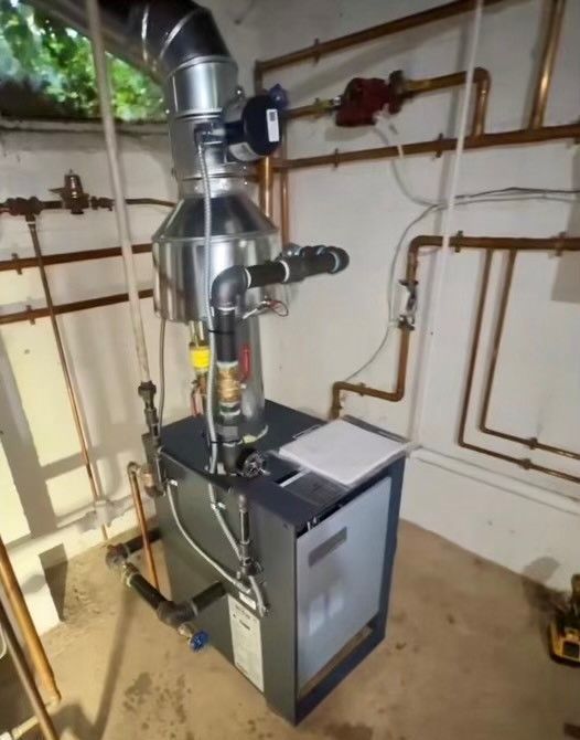 A boiler is sitting in a room surrounded by pipes