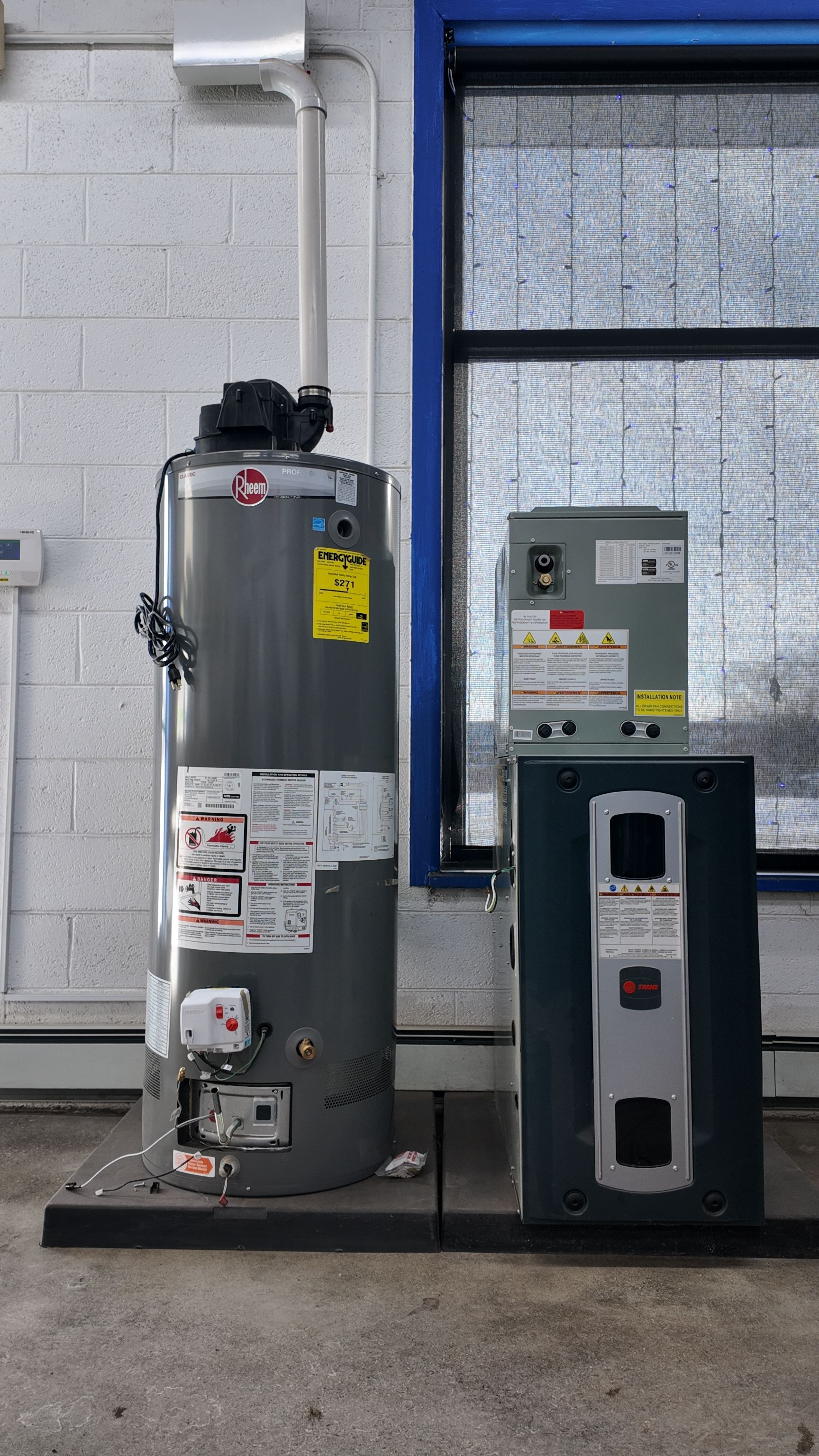 Water heater and attached control panel near a window in a utility room. Gray and black.