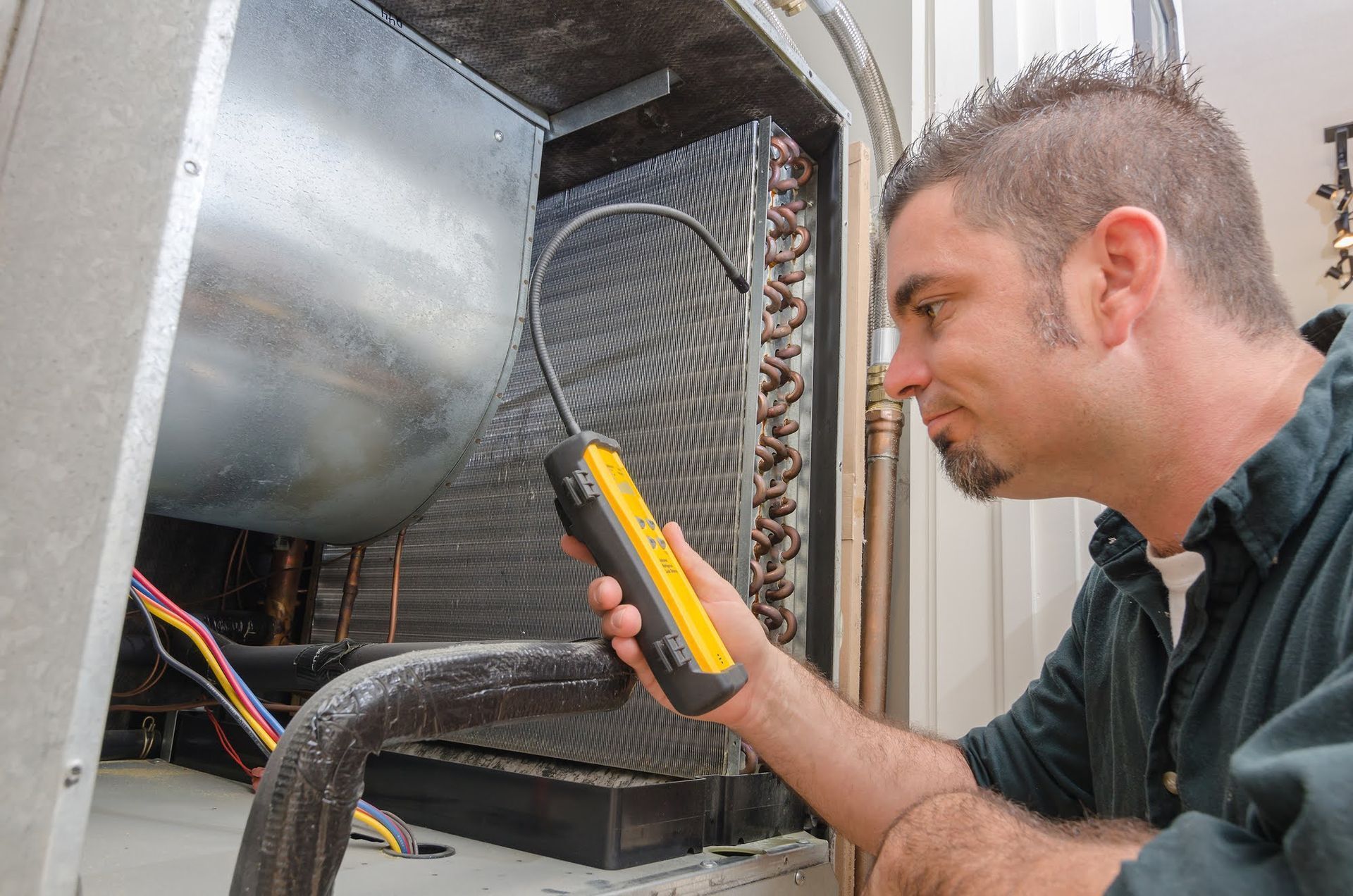 A man is working on an air conditioner with a hose attached to it.
