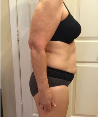 A woman in a black bra and grey underwear is standing in front of a white door.