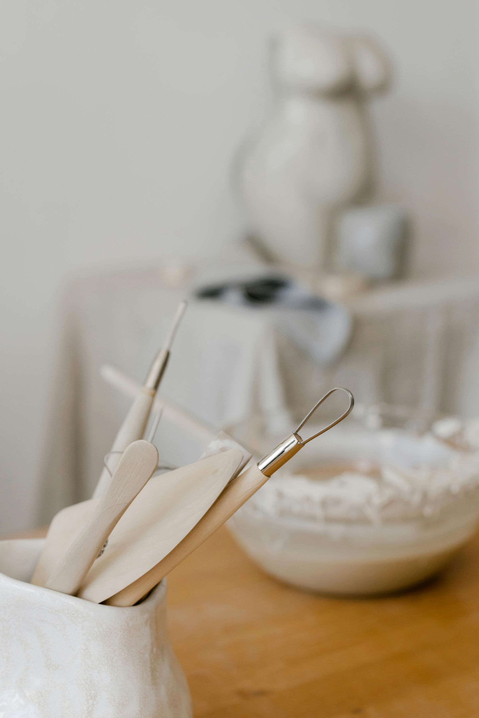 A vase filled with clay utensils is sitting on a wooden table.
