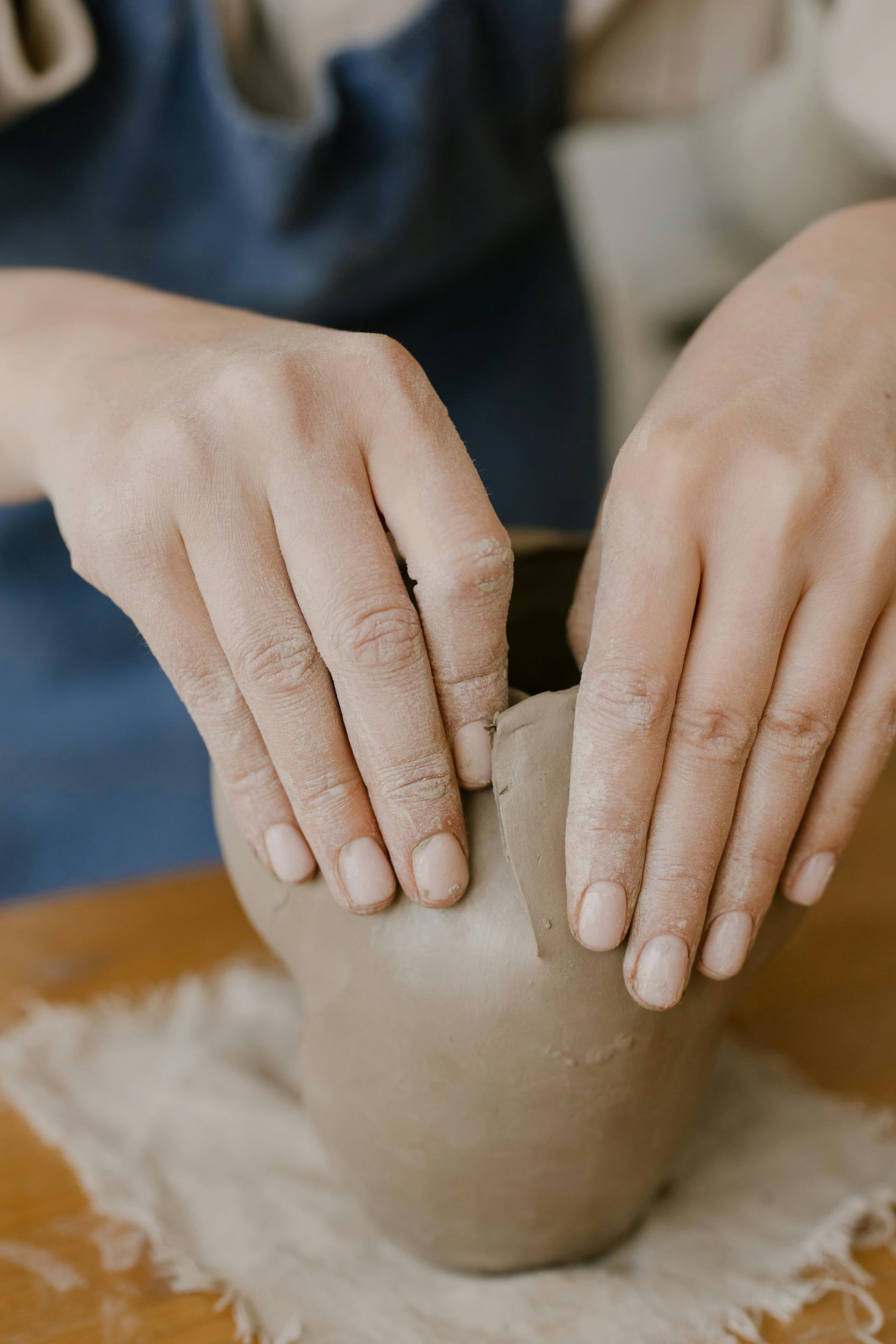A person is making a vase out of clay on a table.