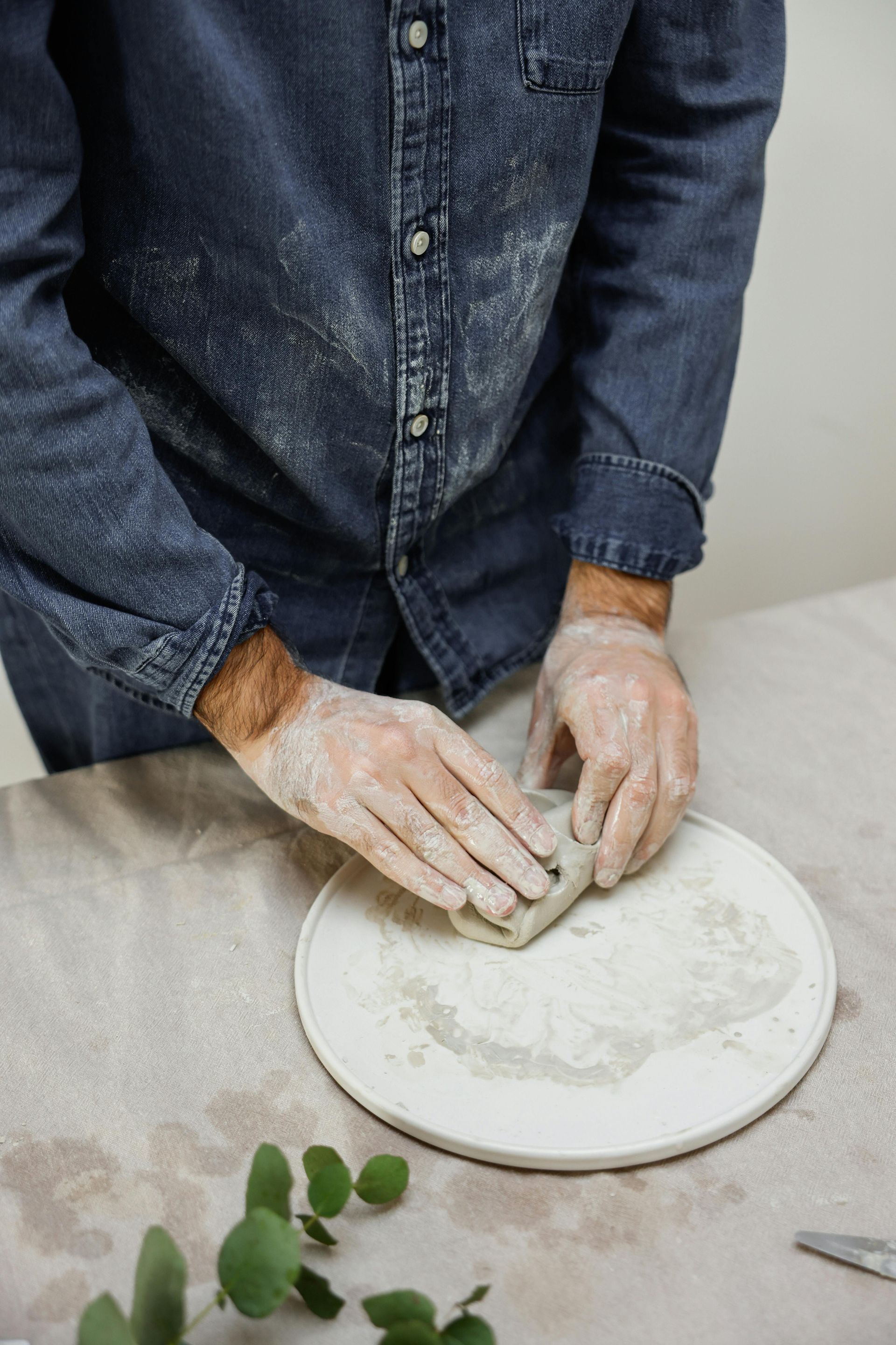 A man wearing gloves is holding a piece of clay on a plate.