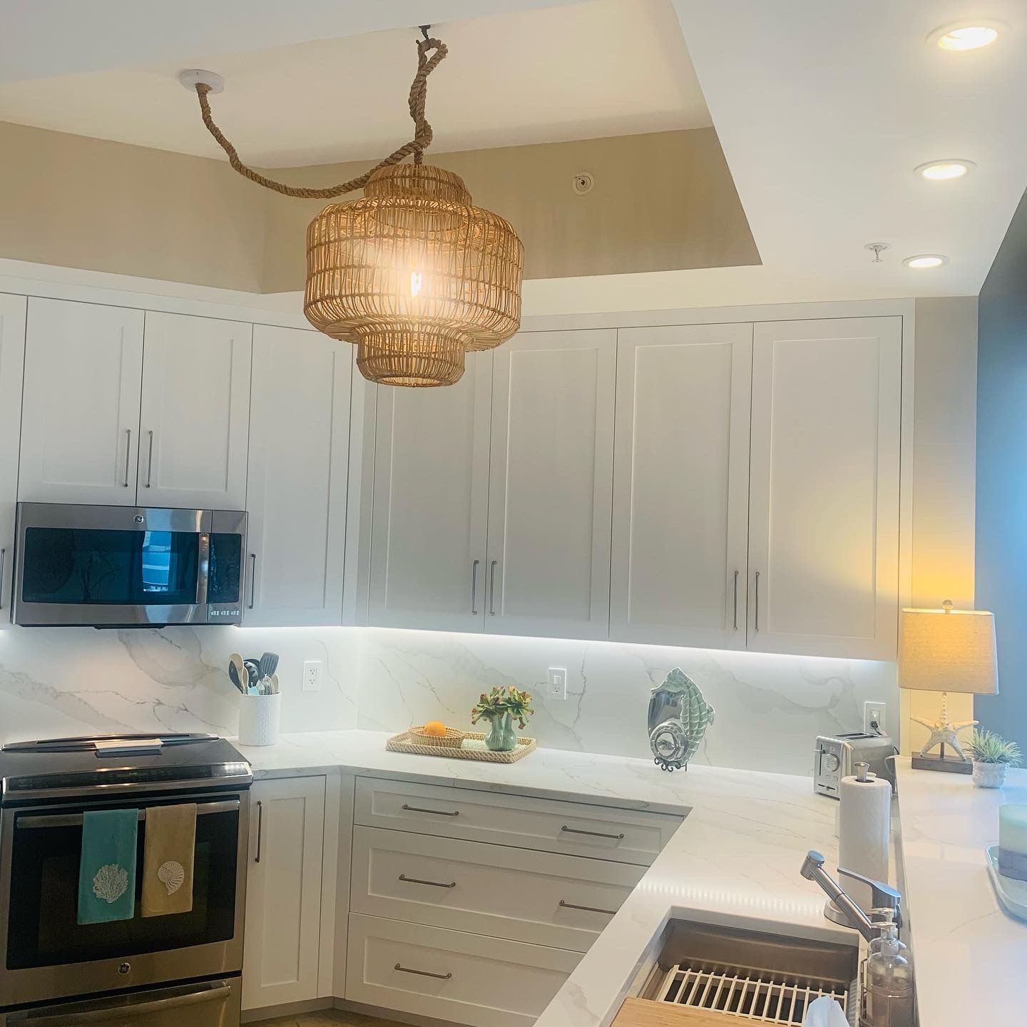 A kitchen with white cabinets and a wicker chandelier hanging from the ceiling