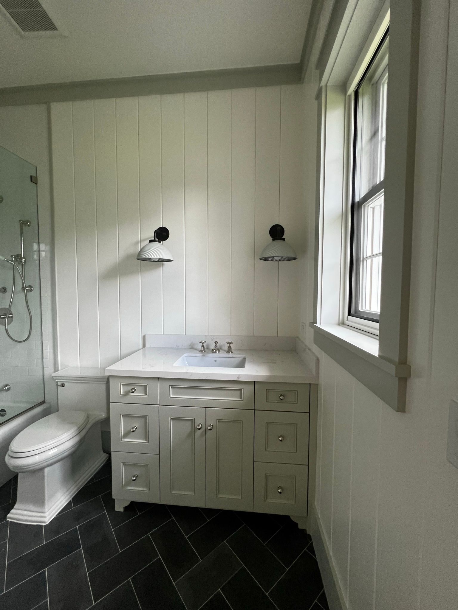 A bathroom with a sink , toilet , shower and window.