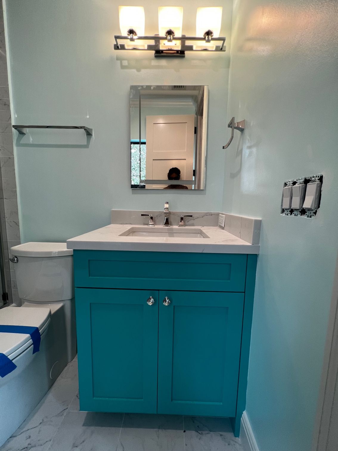 A bathroom with a blue vanity , toilet , and mirror.