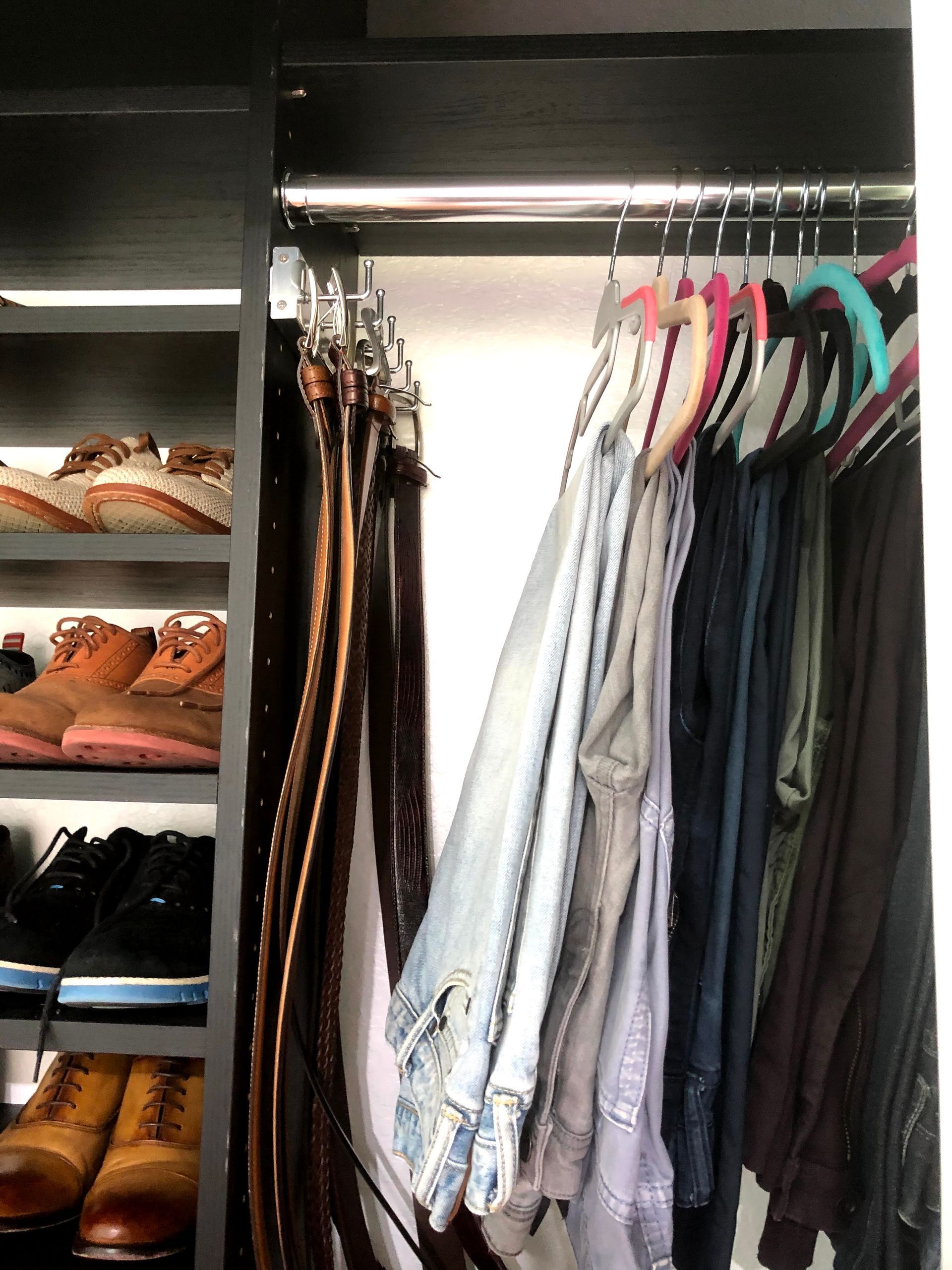 A closet filled with clothes and shoes including a pair of brown boots