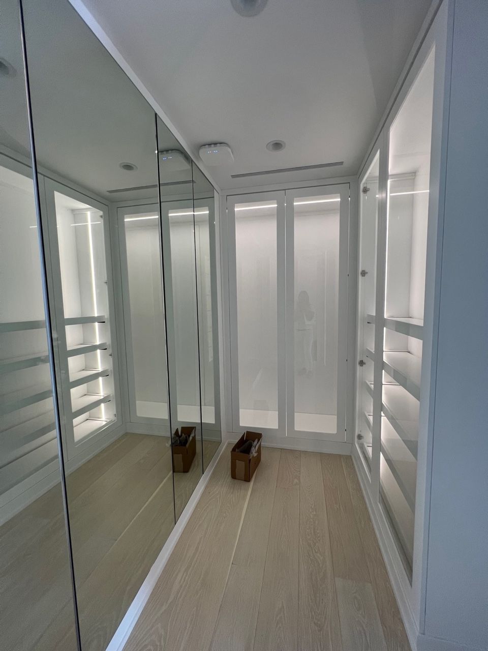 A walk in closet with lots of shelves and mirrors.