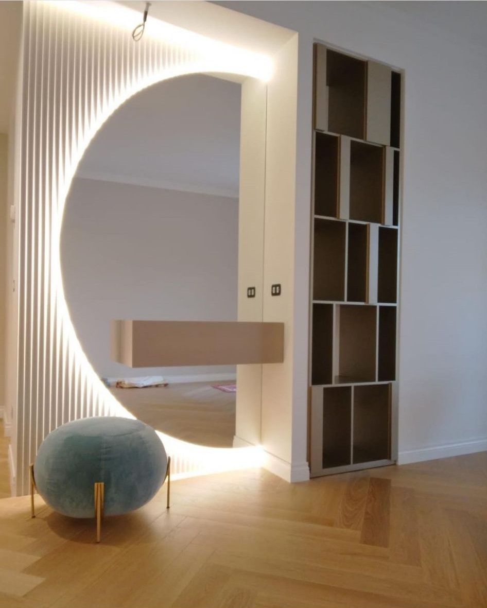 Specchio circolare con illuminazione integrata e piccola mensola; pouf color verde acqua. Scaffale integrato a destra.