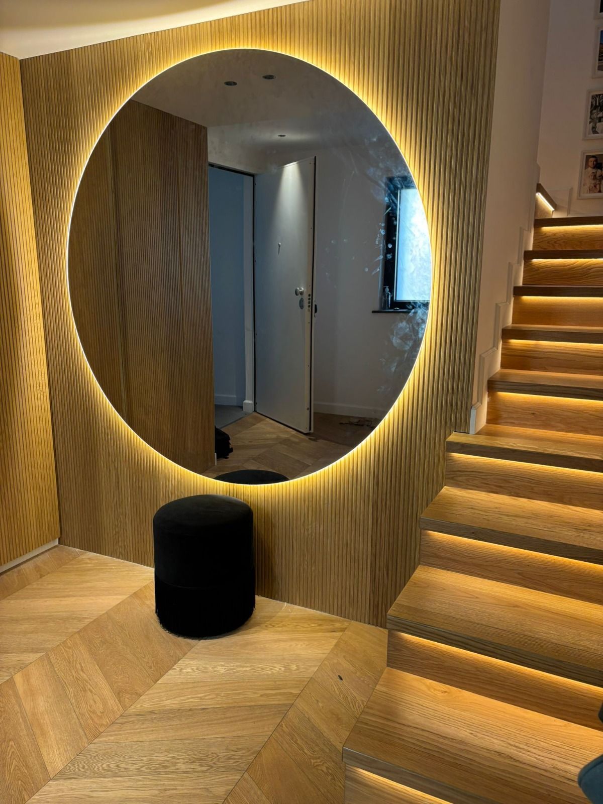 Specchio rotondo con bordo luminoso su pannelli in legno, sgabello e scale con luci integrate.