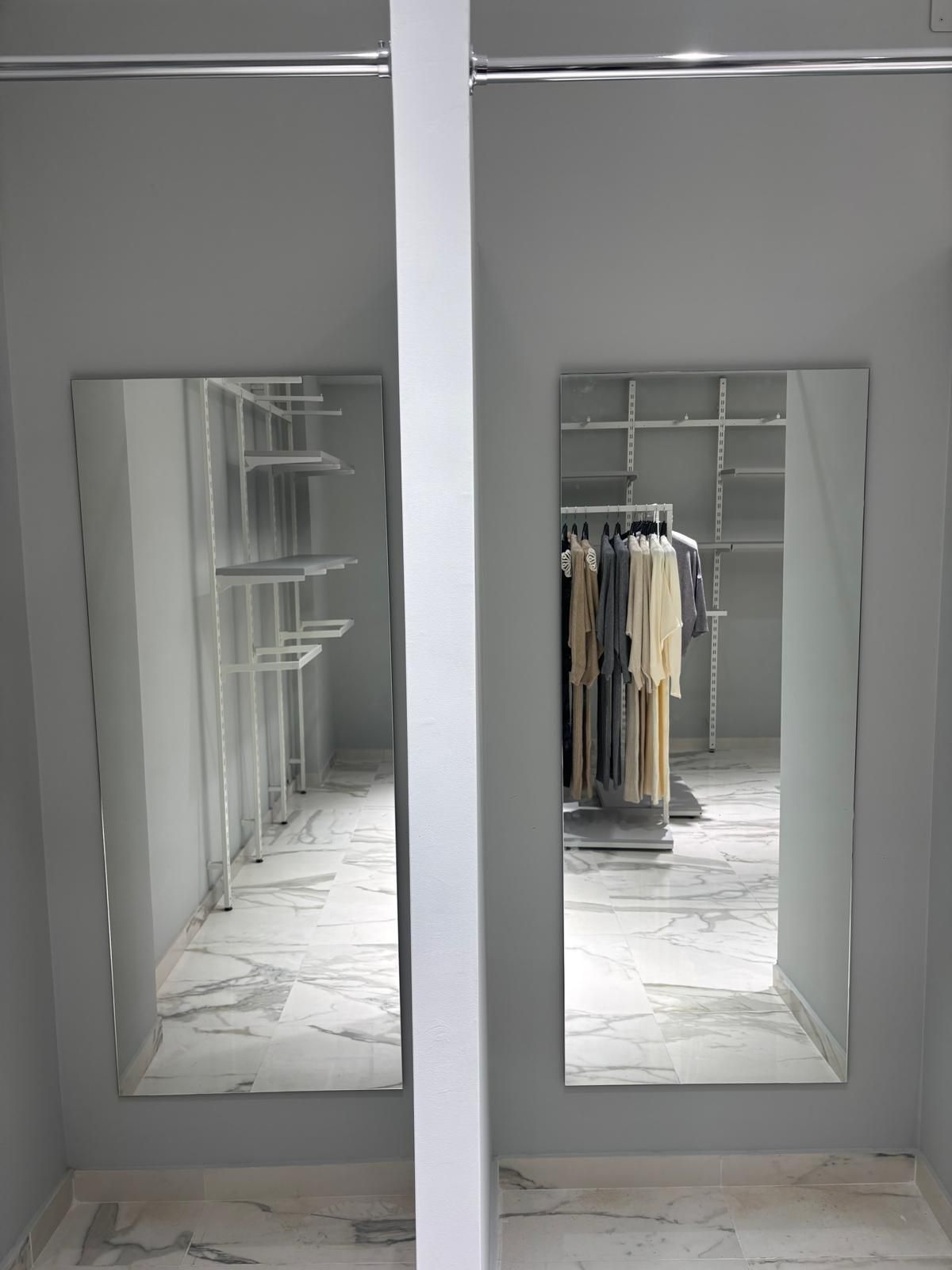 Gli specchi riflettono l'interno di un negozio di abbigliamento con abiti appesi, scaffali e un pavimento in marmo.