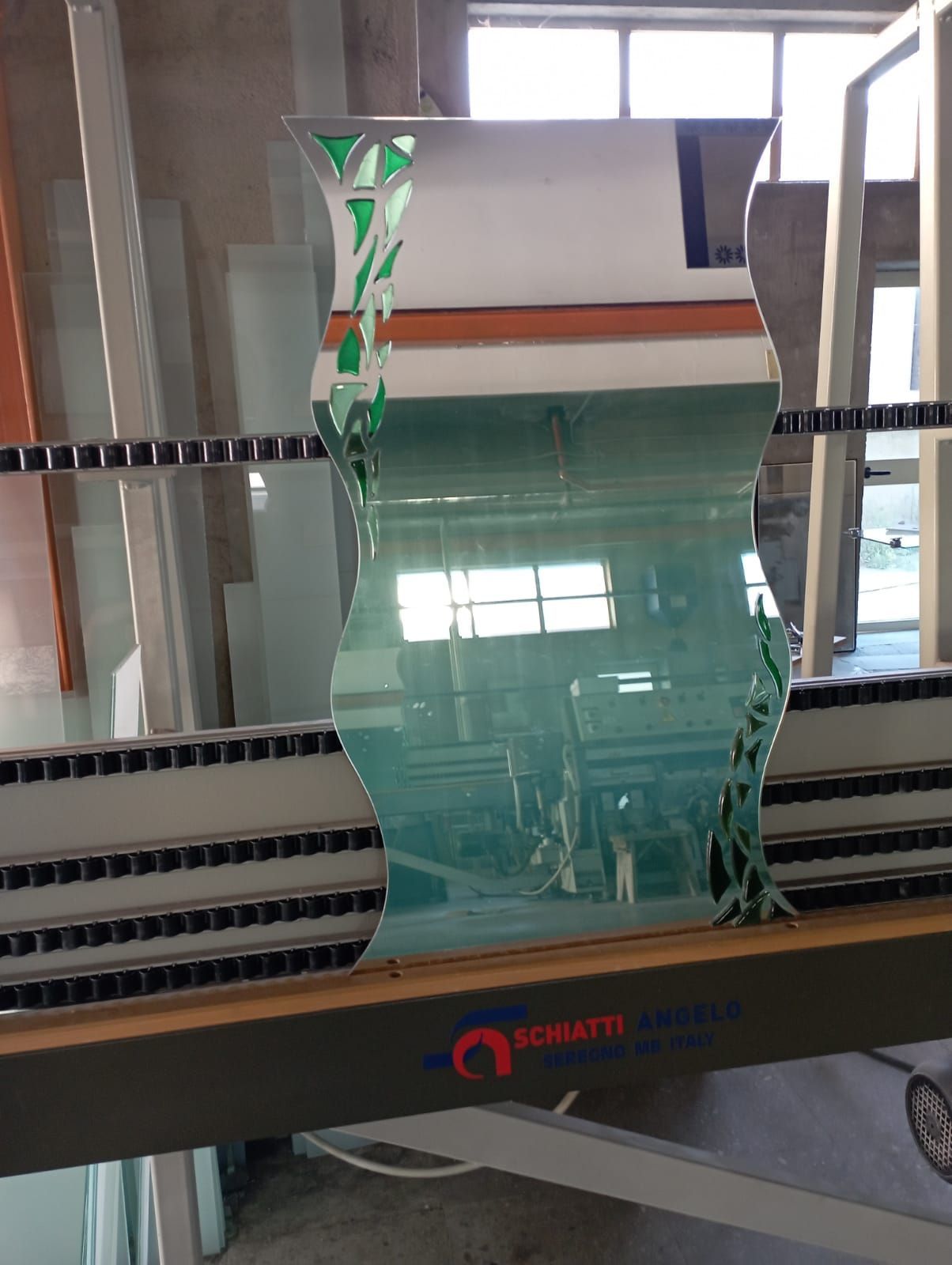 Un pezzo di vetro ondulato in uno stabilimento di produzione, con accenti verdi e arancioni, fissato su una macchina.