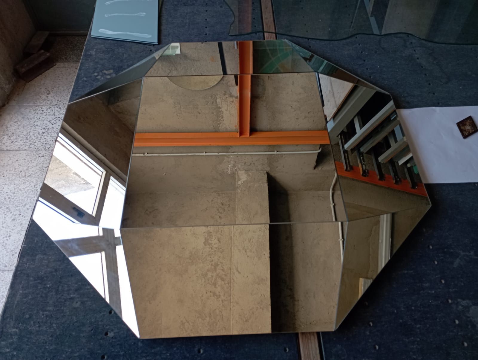 Specchio ottagonale su una superficie scura, che riflette una stanza con tubi arancioni.