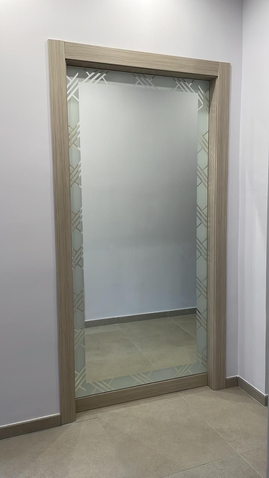 Specchio a figura intera con bordo decorato in una stanza con pareti grigio chiaro.